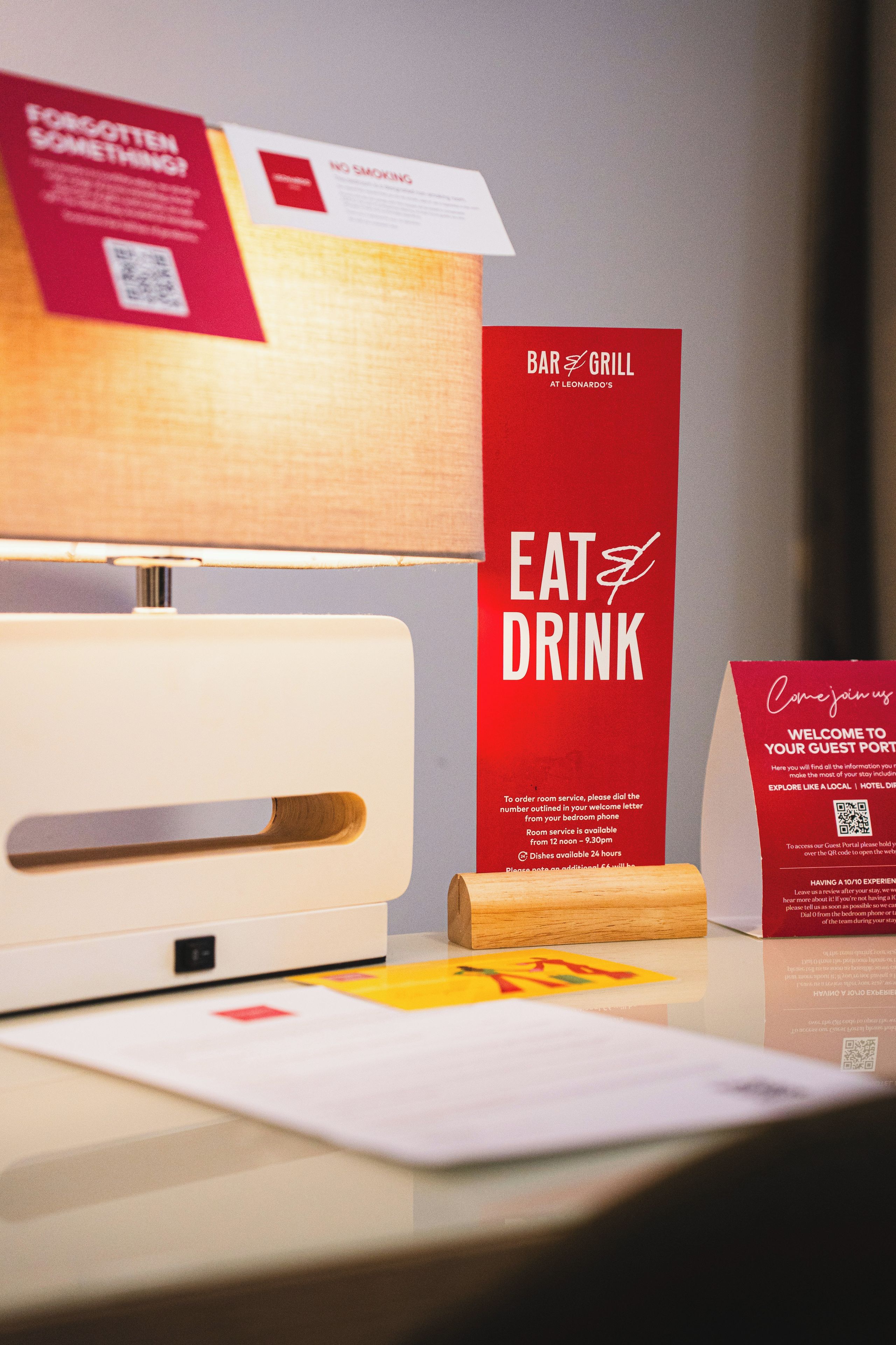 A hotel reception desk with a red sign that reads 'EAT & DRINK' and a 'NO SMOKING' sign above it.