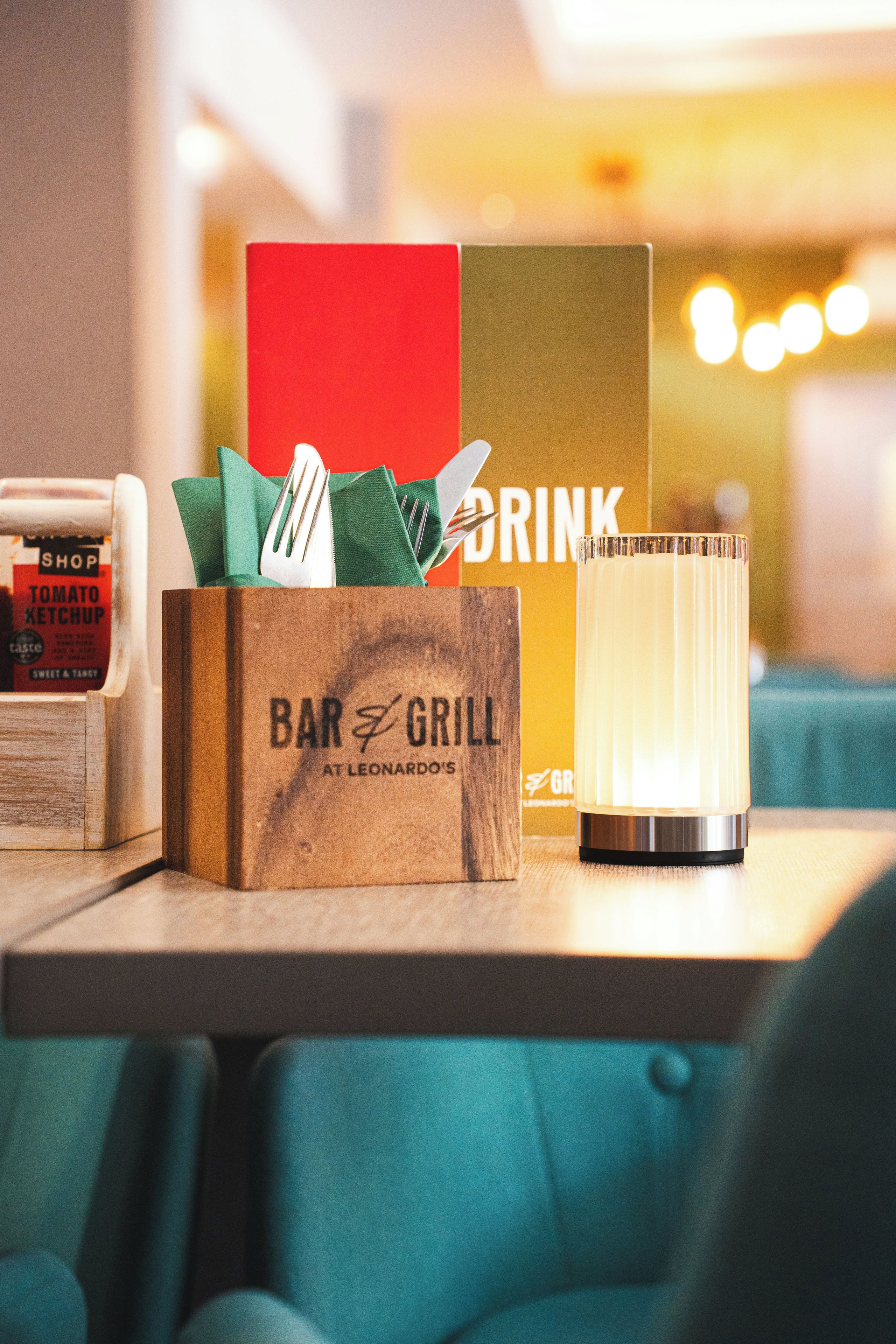 A bar and grill sign with a bottle of ketchup and a drink glass on a table.