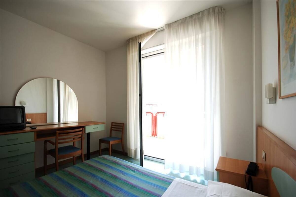 Ein Hotelzimmer mit einem Bett, einem Schreibtisch mit Stuhl, einem Fernseher und einem Fenster mit Vorhängen.