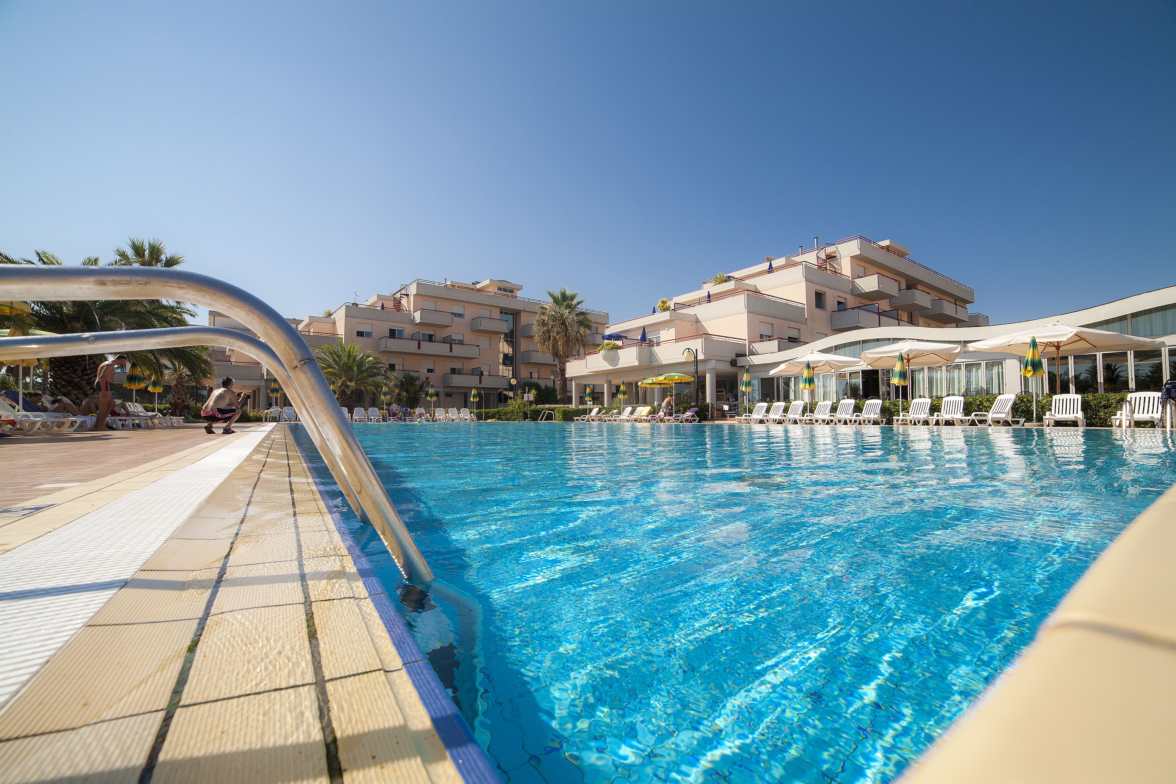 Une piscine entourée de bâtiments dotés de balcons, avec des chaises longues et des parasols à proximité.