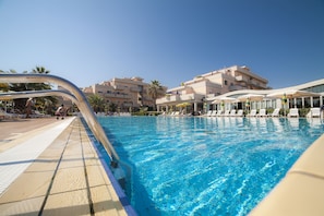 Ein Schwimmbecken mit Liegestühlen und Sonnenschirmen, umgeben von Gebäuden mit Balkonen.