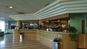 Un hall d’hôtel doté d’un comptoir d’accueil incurvé, d’un bar et d’un espace salon avec des fauteuils.