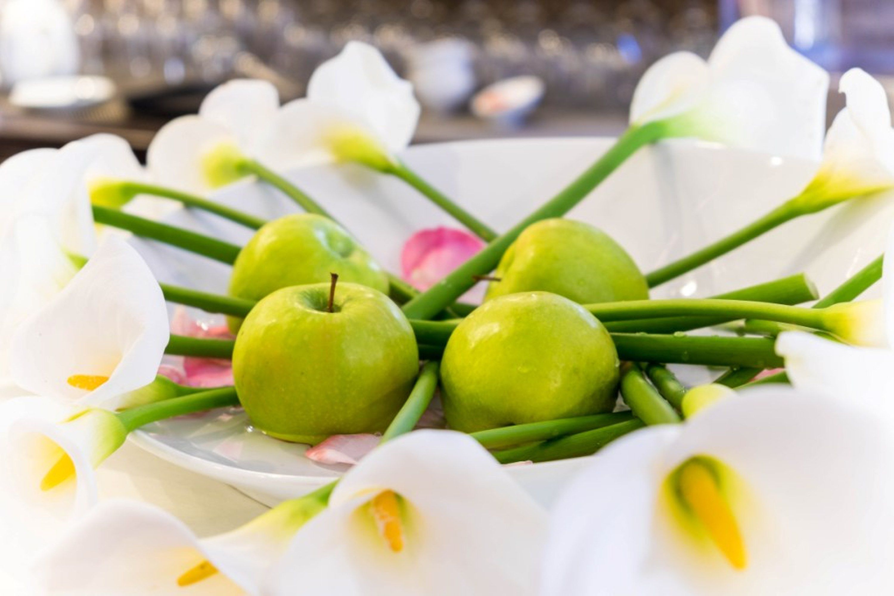 A bowl of green apples surrounded by white flowers.