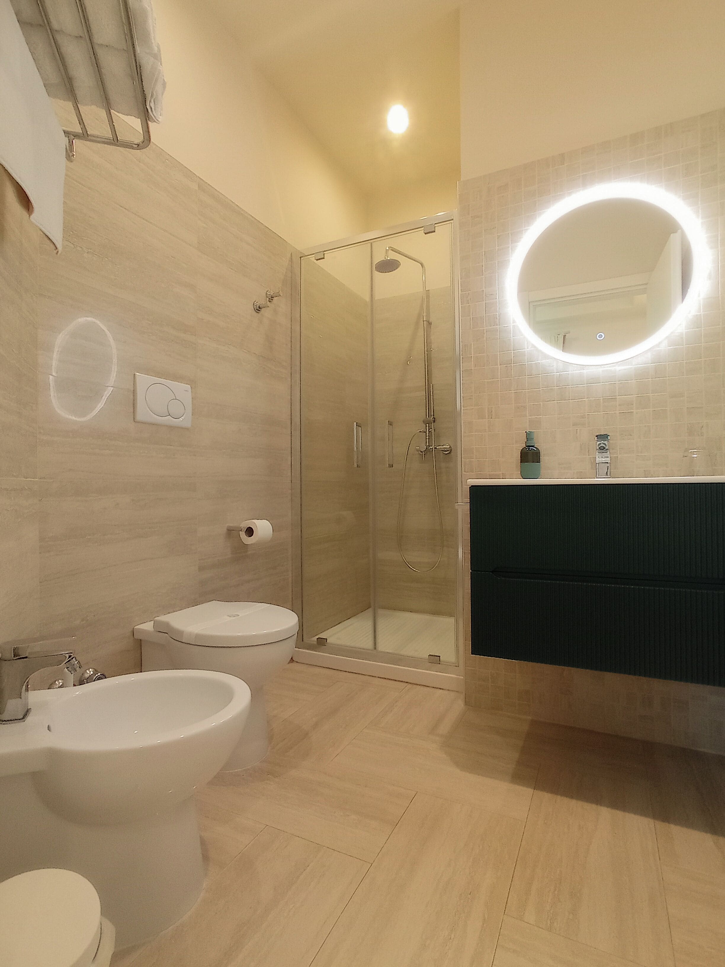 Ein modernes Badezimmer mit einer Duschkabine, einer weißen Toilette, einem Bidet und einem Waschtisch mit Spiegel.