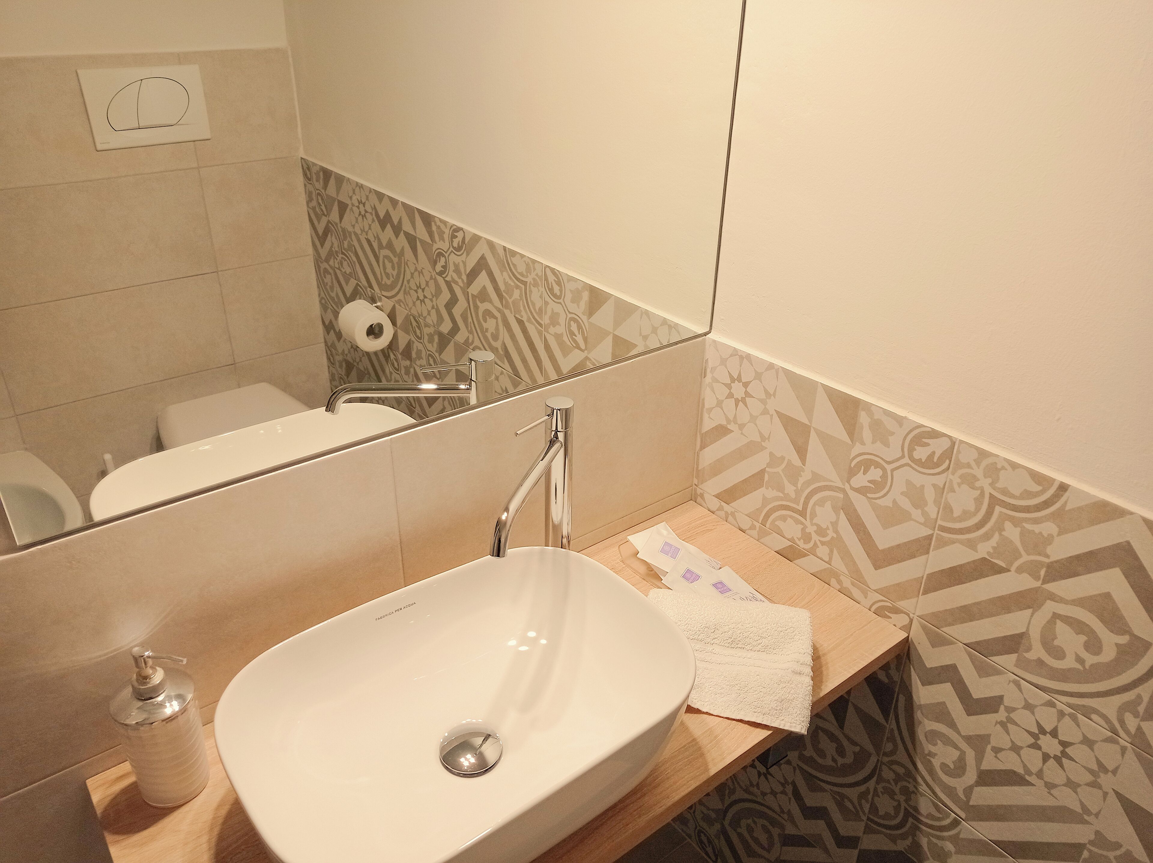 A bathroom with a white sink, a mirror, a toilet, and patterned tiles.