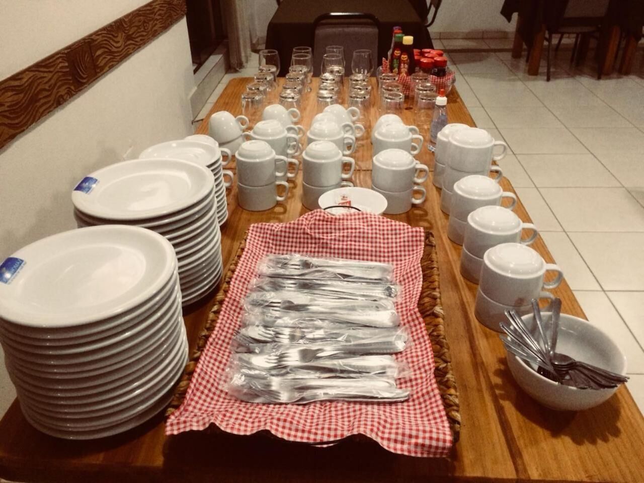 A dining table with stacked plates, cups, and utensils.