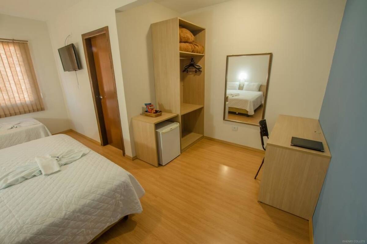 Une chambre d’hôtel avec deux lits, une armoire, un petit bureau, un miroir et un téléviseur.
