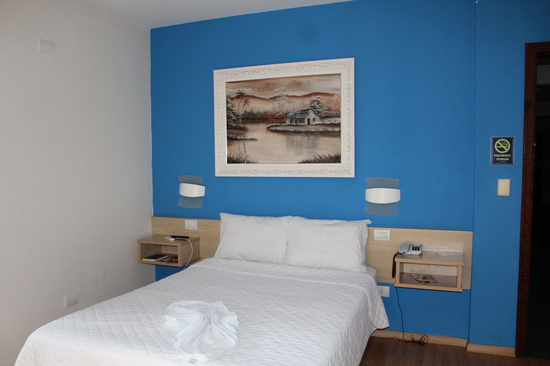 A hotel room with a bed, a painting on the wall, bedside lamps, and a nightstand with a phone.