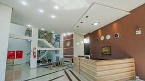 A modern reception area with a staircase, a reception desk, and a wall with clocks and a framed certificate.