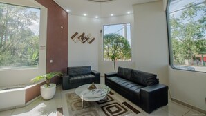 A modern living room with two black leather sofas, a glass coffee table, and a potted plant.
