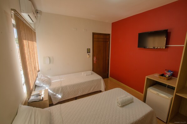 A hotel room with two beds, a TV, a small refrigerator, and a window with curtains.