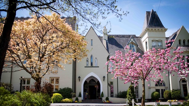 Un edificio grande e histórico con una entrada destacada, rodeado de jardines y árboles bien cuidados.
