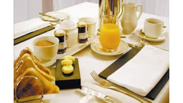 Et morgenbord dækket til to personer, med tallerkener, skåle, kande, kop og et glas appelsinjuice.