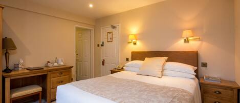 A hotel room with a large bed, bedside tables, a desk with a chair, and a lamp.