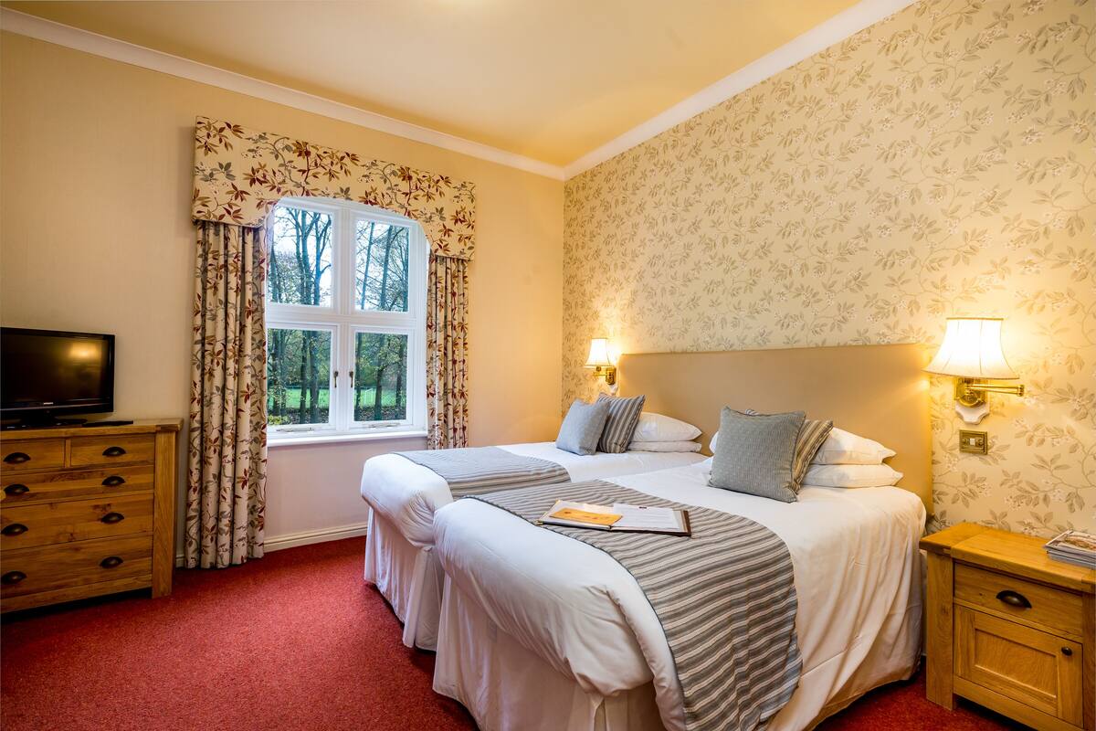 Een hotelkamer met twee bedden, een televisie, een houten dressoir en een raam met gordijnen.