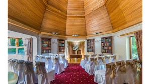 Una habitación con techo de madera alto, alfombra roja y filas de sillas cubiertas de blanco y lazos.