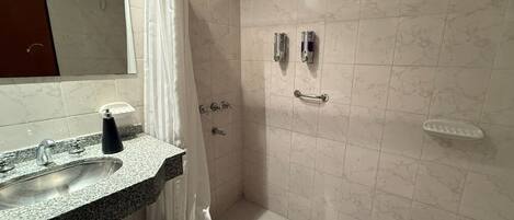 A bathroom with a sink, mirror, shower, and tiled walls.