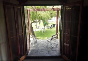 Una puerta abierta que da a un patio con suelo de piedra, dos bancos y un árbol.