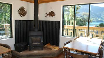 A cozy room with a wood-burning stove, wooden furniture, and large windows offering a view of the outdoors.