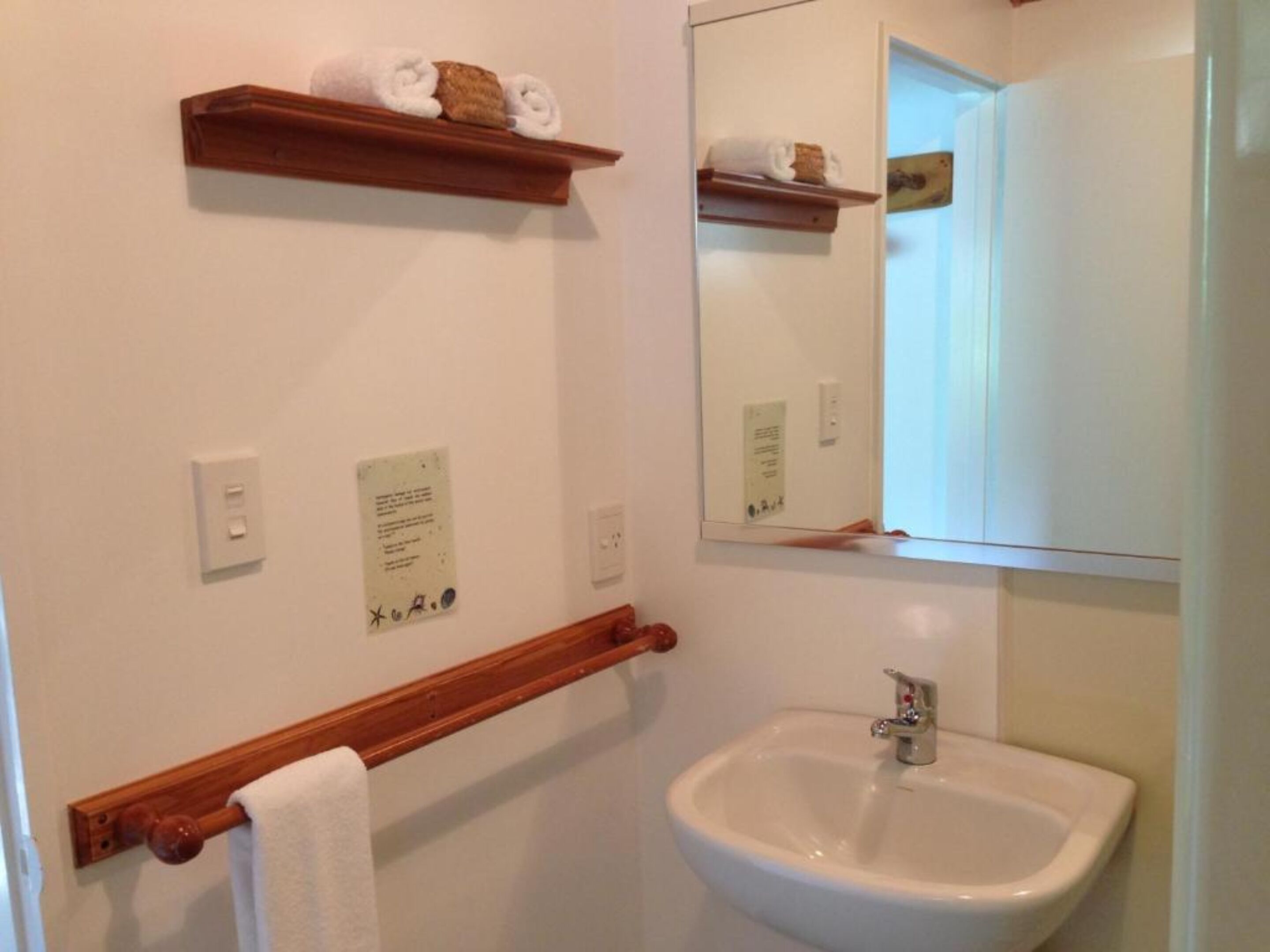 A bathroom with a white sink, wooden towel rack, and a mirror above it.