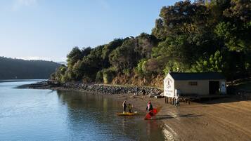 A lakeside scene with a small building, a sandy beach, and people near canoes.