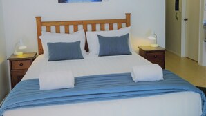A neatly made bed with a blue and white striped bedspread, two pillows, and two folded towels. There is a painting of a beach scene on the wall above the bed. - Lochmara Lodge (Lochmara Bay)