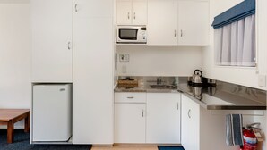 A compact kitchen with white cabinets, a microwave, a kettle, and a small refrigerator. - Lochmara Lodge (Lochmara Bay)