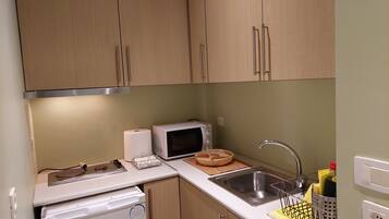 A compact kitchen with wooden cabinets, a microwave, a sink, and a washing machine.