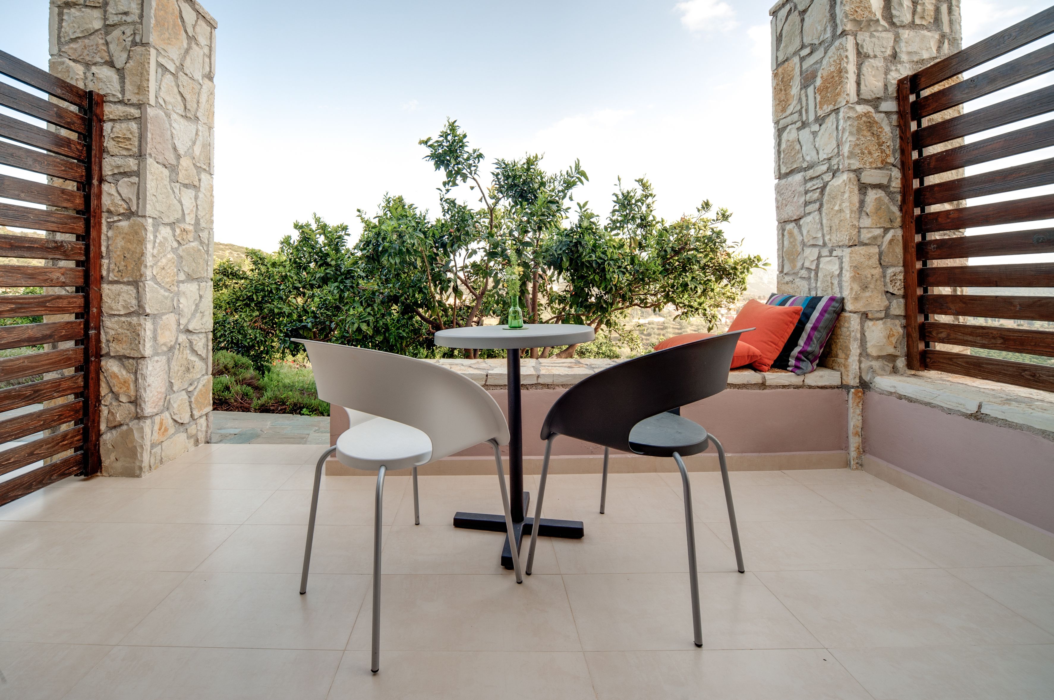 Un espace patio avec une table ronde et deux chaises, des murs en pierre et une vue sur la verdure.