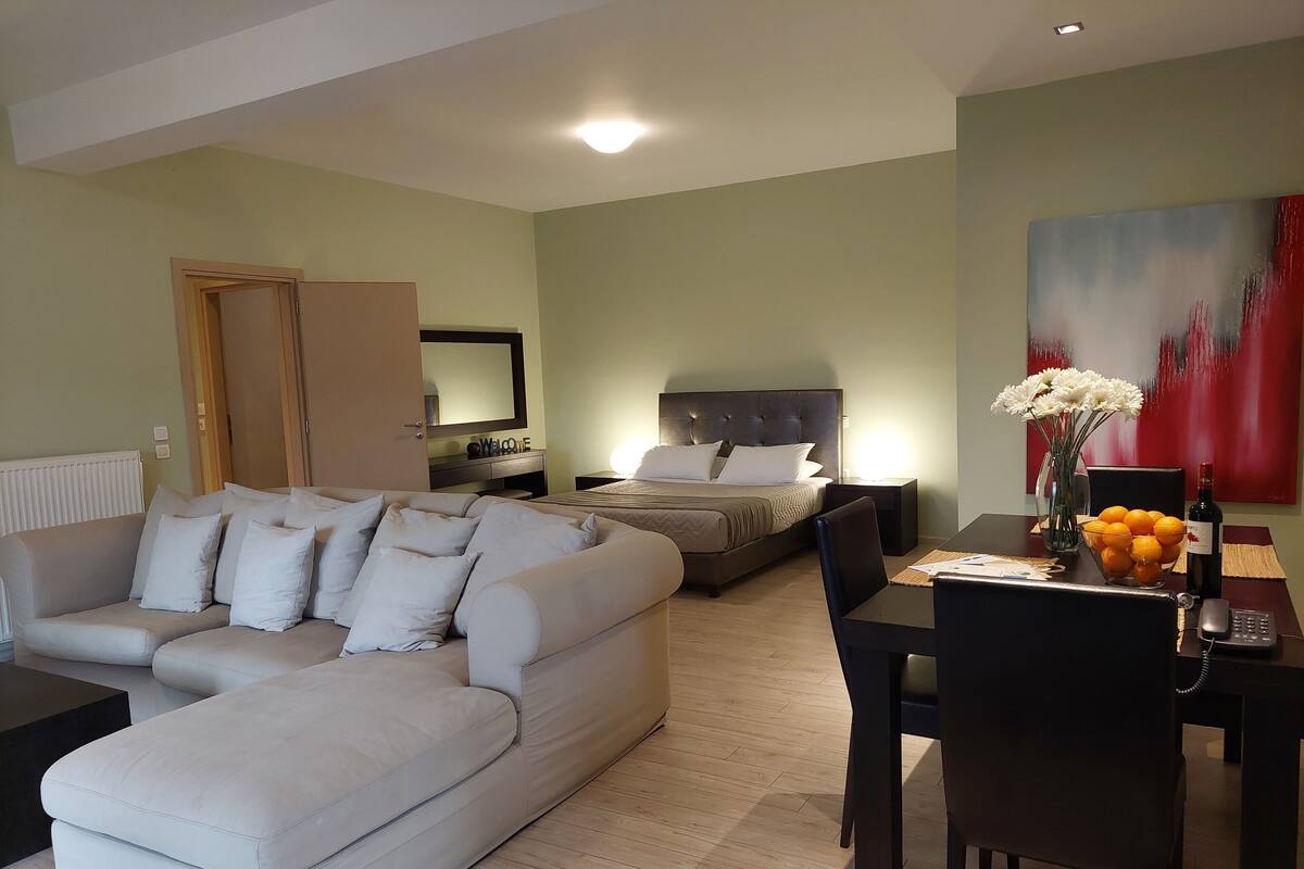 A modern living room with a sofa, a dining table with chairs, a bed with a headboard, and a painting on the wall.