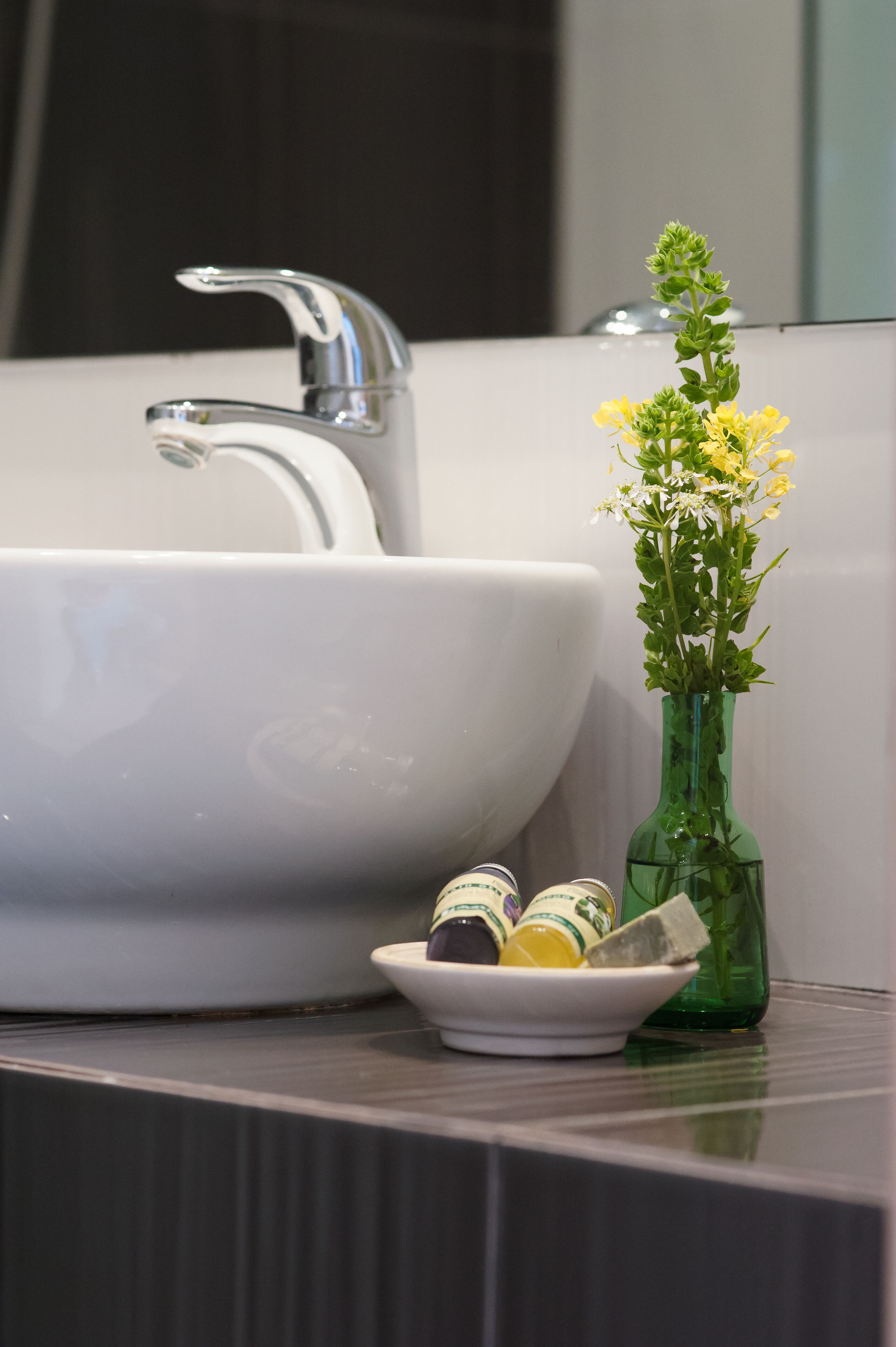 Un lavabo de salle de bain avec un vase vert contenant des fleurs jaunes et un petit récipient avec du savon.