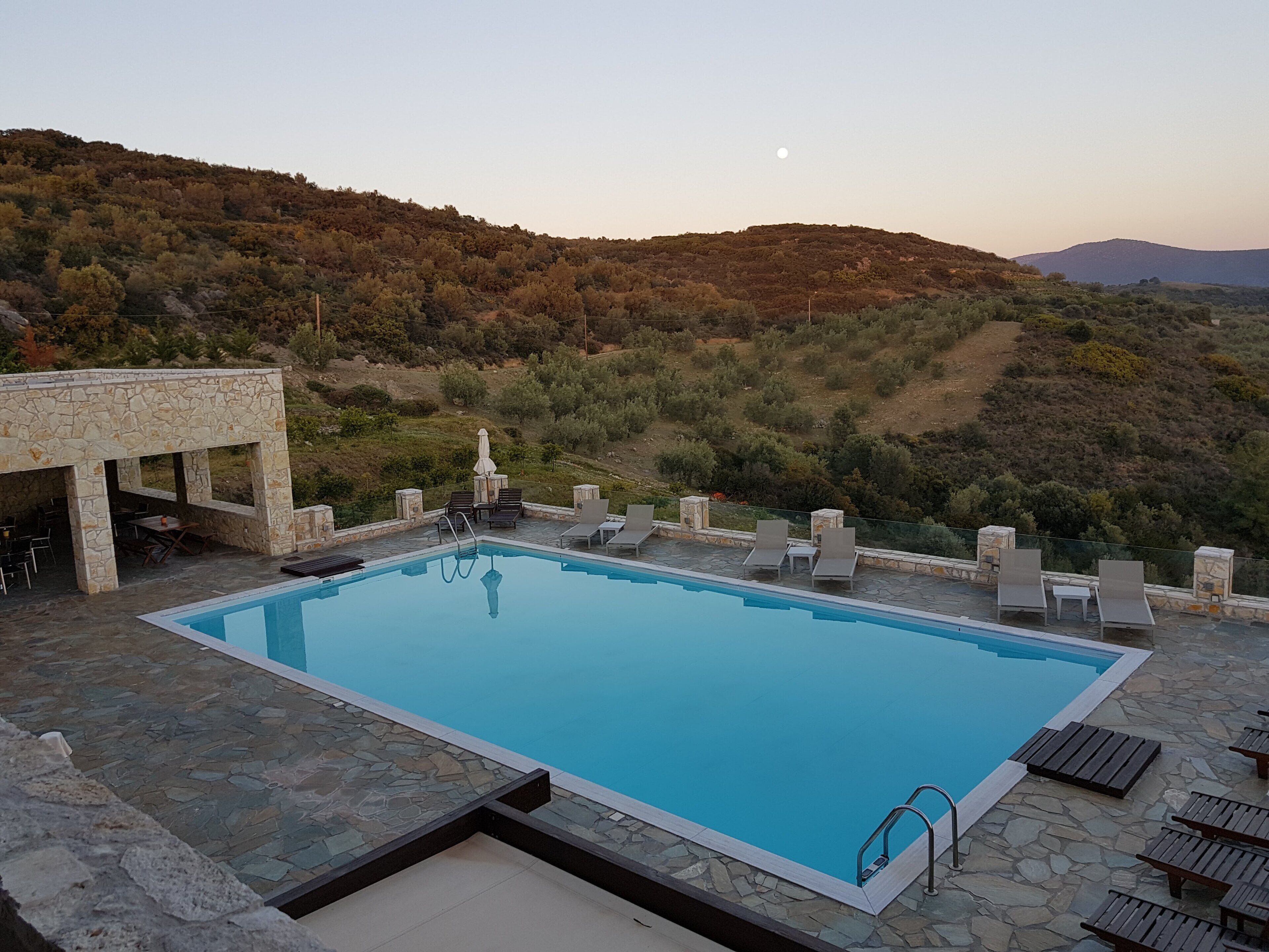 A swimming pool with lounge chairs and a stone structure, surrounded by a hilly landscape.