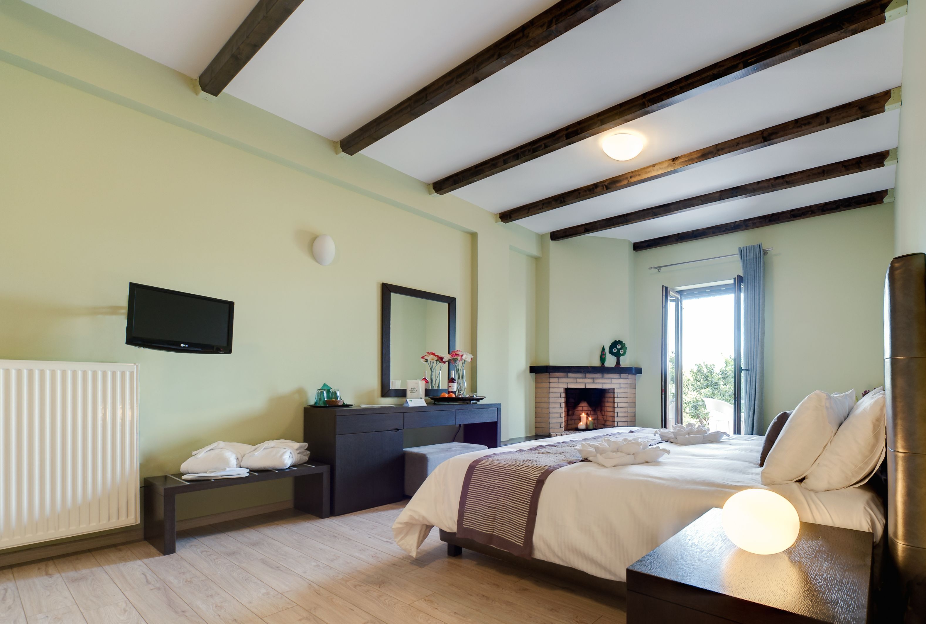 A bedroom with a bed, bedside table, dresser, mirror, fireplace, and a TV mounted on the wall.