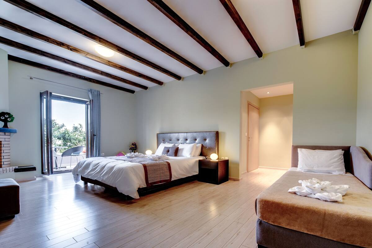 A bedroom with a large bed, a smaller bed, a nightstand, and a window with curtains.