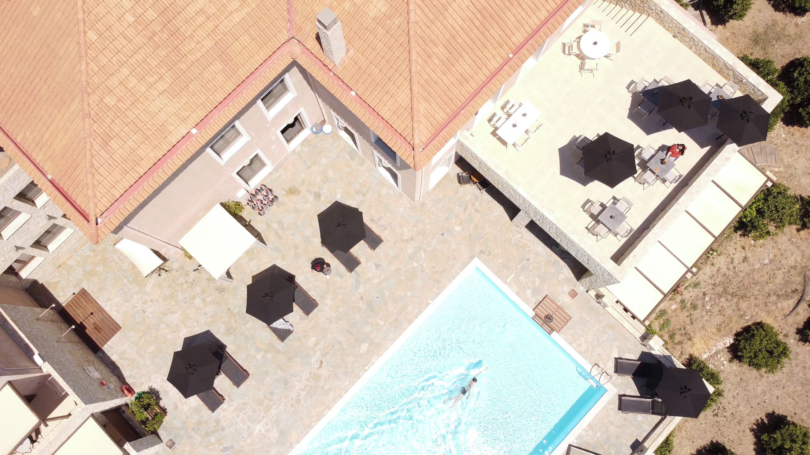 An aerial view of a resort with a swimming pool, sun loungers, umbrellas, and outdoor seating areas.