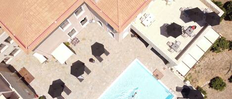 An aerial view of a resort with a swimming pool, sun loungers, umbrellas, and outdoor seating areas.