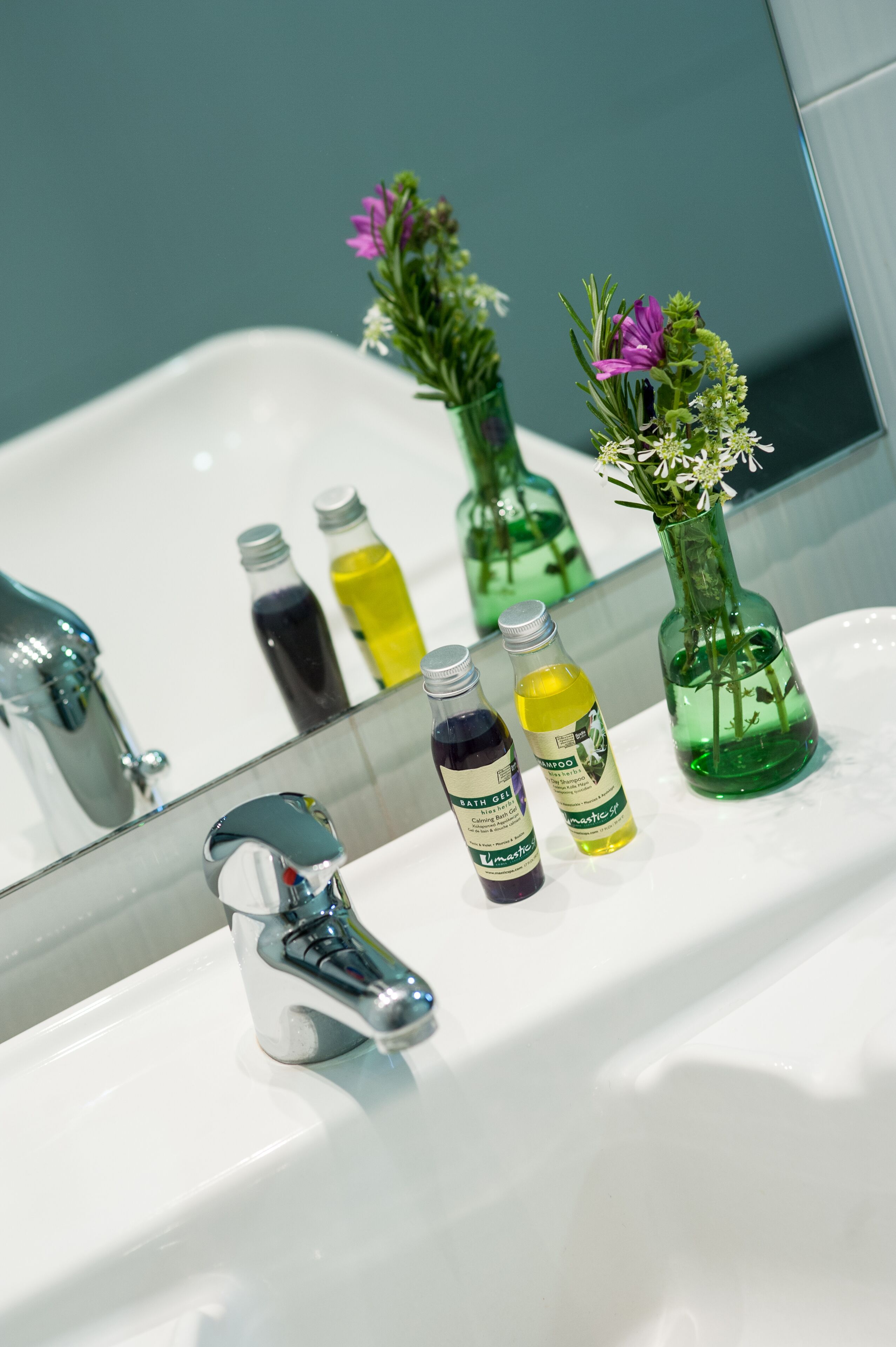 Un lavabo de salle de bain avec un miroir, deux vases avec des fleurs et trois bouteilles de liquide.