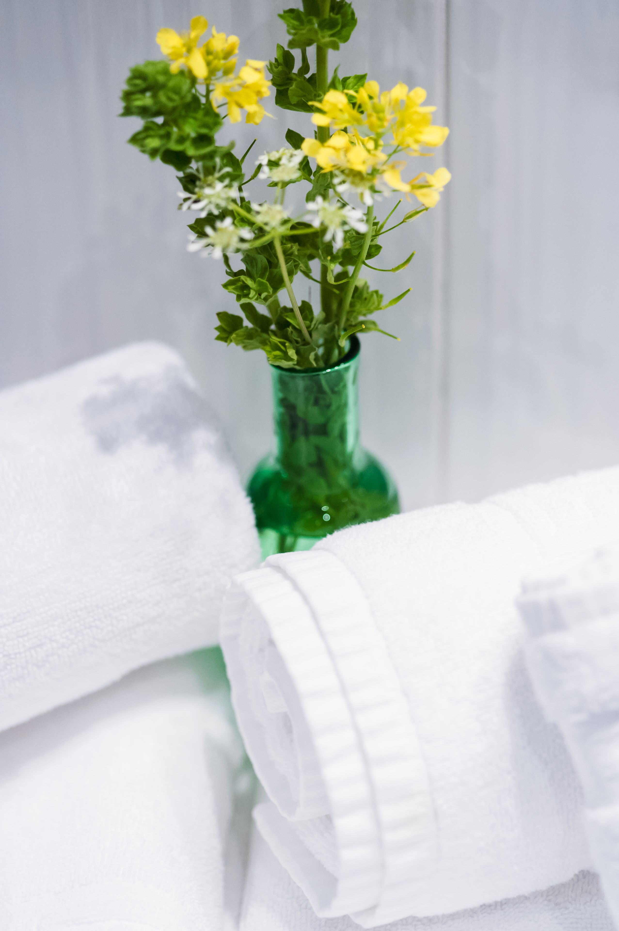 Un vase vert avec des fleurs jaunes et des serviettes blanches.