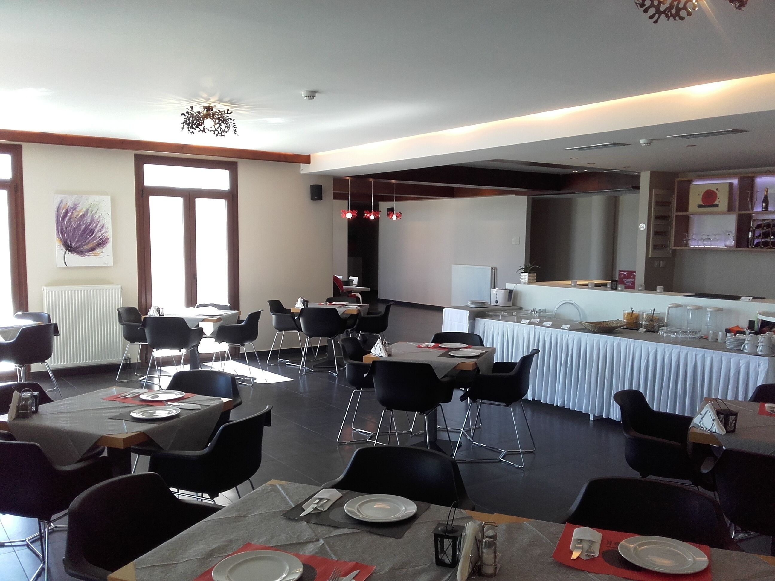 Comedor con mesas dispuestas para el servicio, cocina al fondo y un gran ventanal que proporciona luz natural.