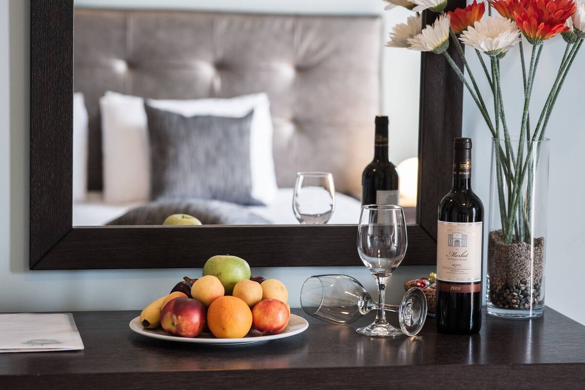 A dining table with a plate of fruit, a wine bottle, a wine glass, and a vase with flowers.