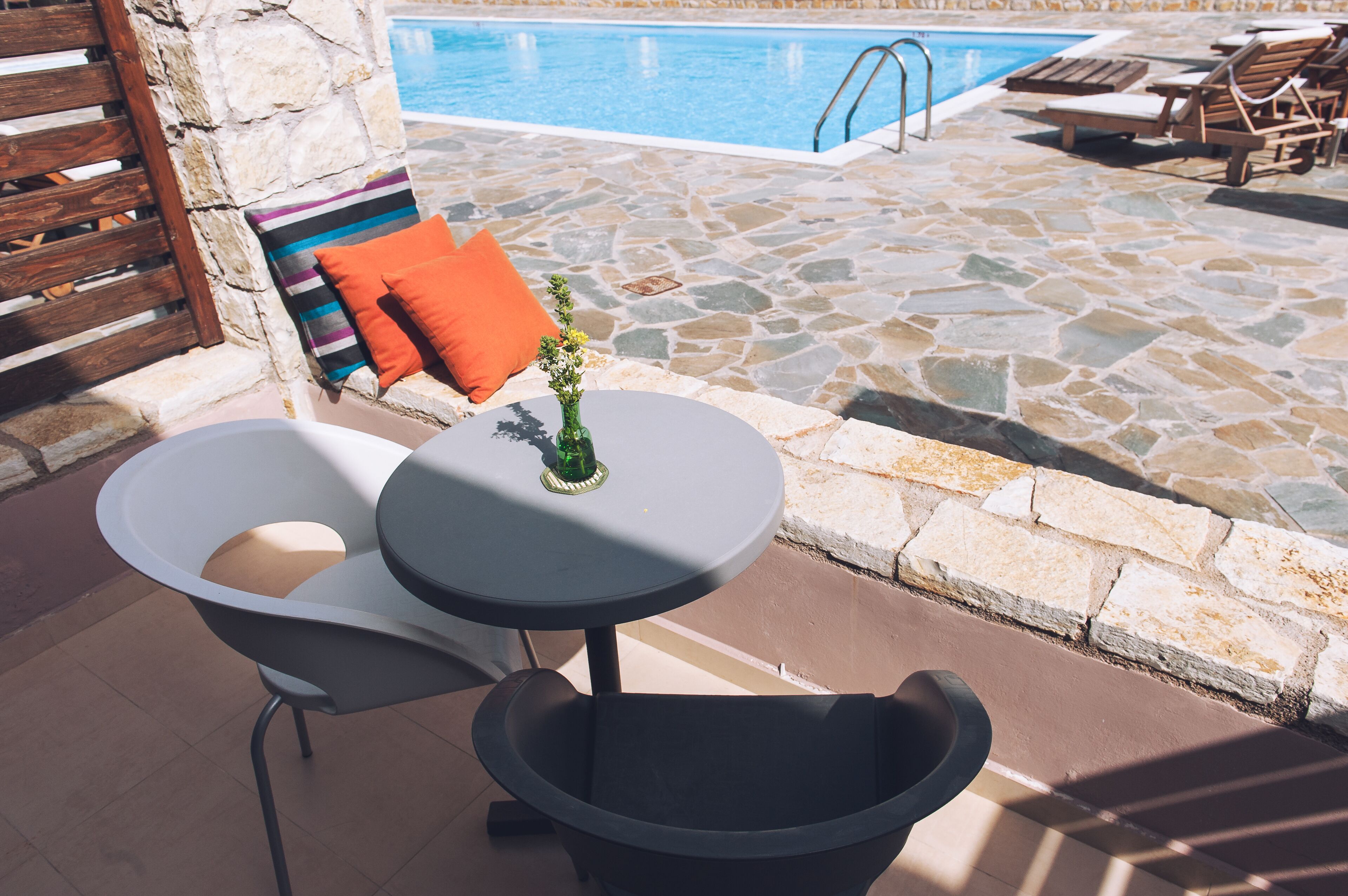 Un espace aménagé au bord de la piscine, avec un sol en pierre, une petite table ronde ornée d’un vase et deux chaises longues.