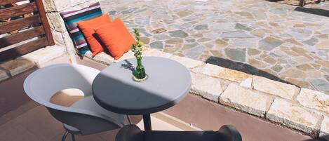 Un espace aménagé au bord de la piscine, avec un sol en pierre, une petite table ronde ornée d’un vase et deux chaises longues.