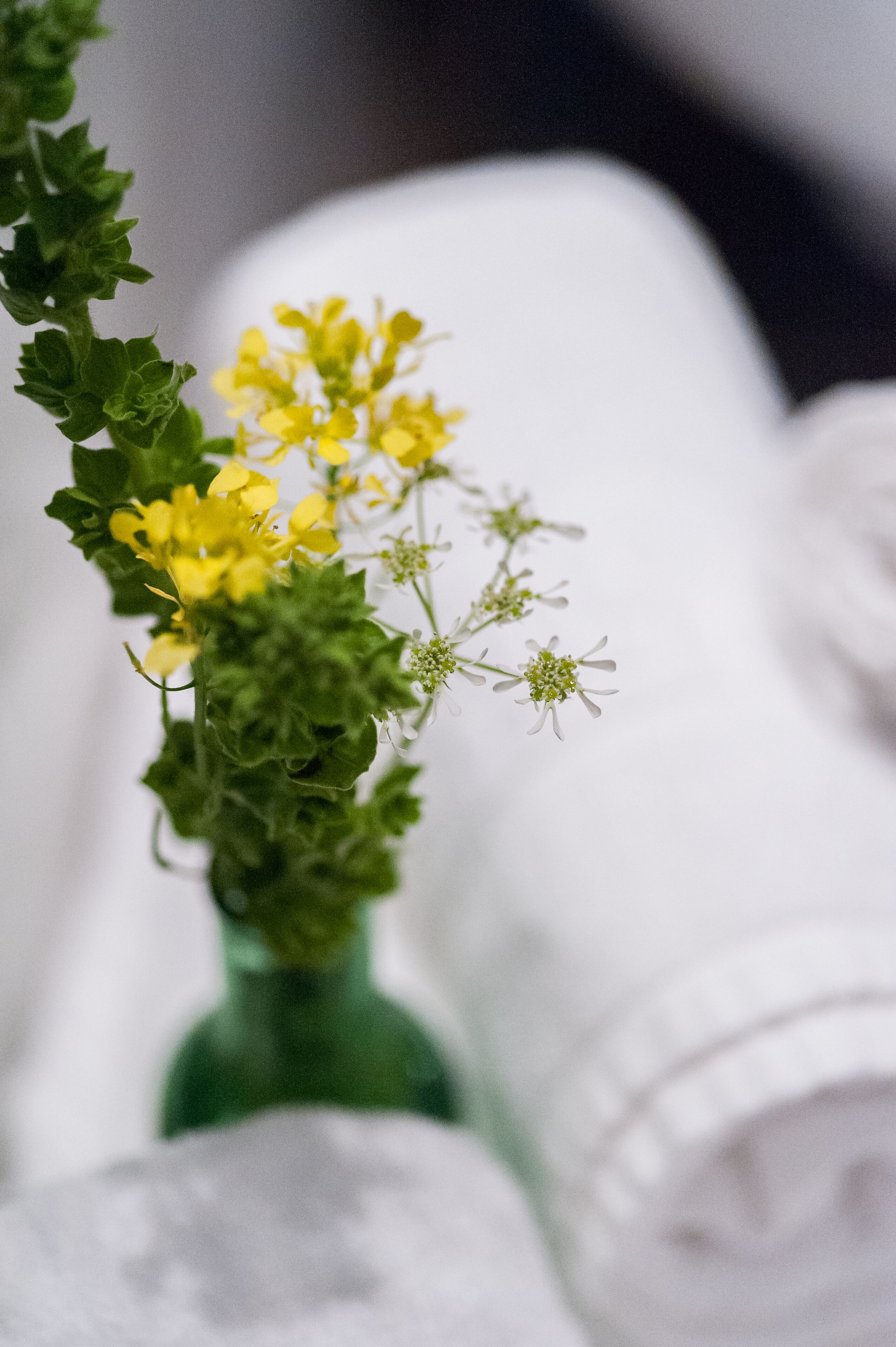 A green vase with yellow flowers and white flowers.