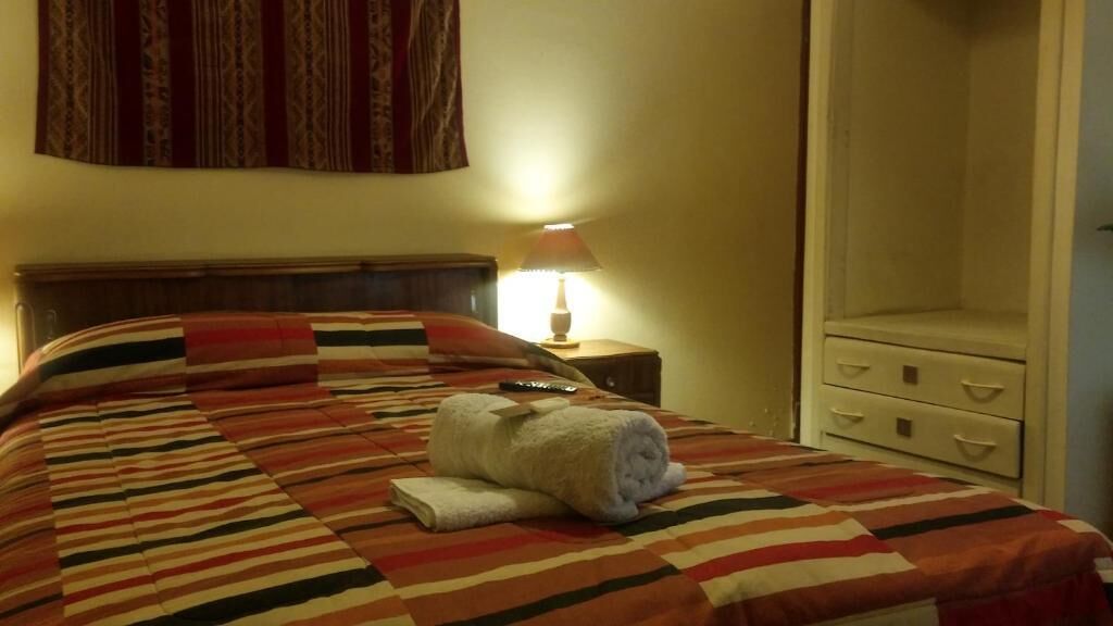 A neatly made bed with a striped blanket, a rolled towel, and a remote control on the nightstand.