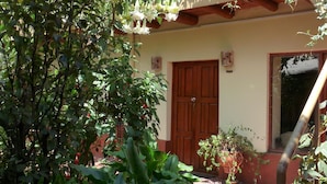 Un patio con plantas en macetas, una puerta de madera y un balcón con plantas.