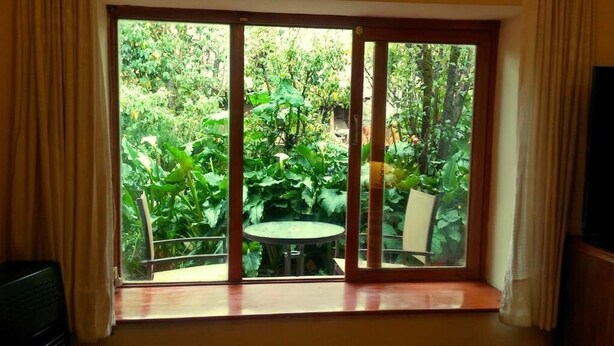 Una habitación con un gran ventanal corredero que da a un balcón con abundante vegetación y una pequeña mesa redonda.