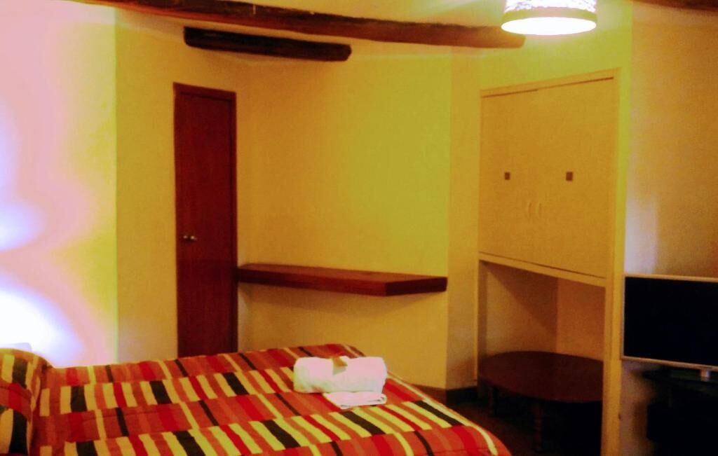 A small room with a bed, a wooden shelf, a wardrobe, and a television.