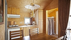 A wooden cabin interior with a dining table, chairs, a kitchen area with a sink, a stove, and a ceiling light fixture. - Legoland Holiday Village (Billund)