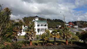 Un edificio blanco con techo verde y una torre, rodeado de palmeras y una carretera.