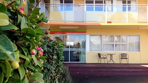 Un hotel de dos pisos con un balcón en el nivel superior, una recepción y una pequeña zona de estar al aire libre.